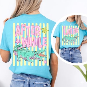 May include: Light blue t-shirts with a graphic of an alligator and the words "AFTER WHILE" and "LATER". The alligator is green with pink accents. The text is pink with yellow and green star accents.