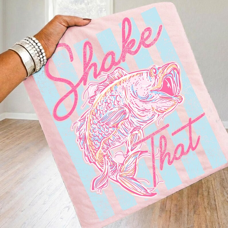 K&ouml;nnte beinhalten: Rosa und blau gestreifte Decke mit einer Fischillustration. Auf der Decke steht in rosa Schrift "Shake That". Der Fisch ist in Rosa-, Blau- und Gelbt&ouml;nen gehalten.