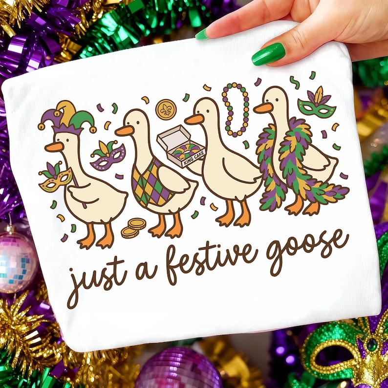 Op de afbeelding: Wit T-shirt met een cartoon illustratie van vier ganzen in Mardi Gras kostuums. De ganzen dragen maskers, kralen en een gevederde boa. De tekst "just a festive goose" is geschreven in een scriptlettertype.