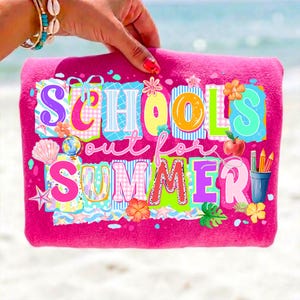 May include: A bright pink beach towel with the words "SCHOOL'S out for SUMMER" in colorful, playful lettering. The design includes images of a globe, apple, pencils, and flowers. The towel is held up by a person.
