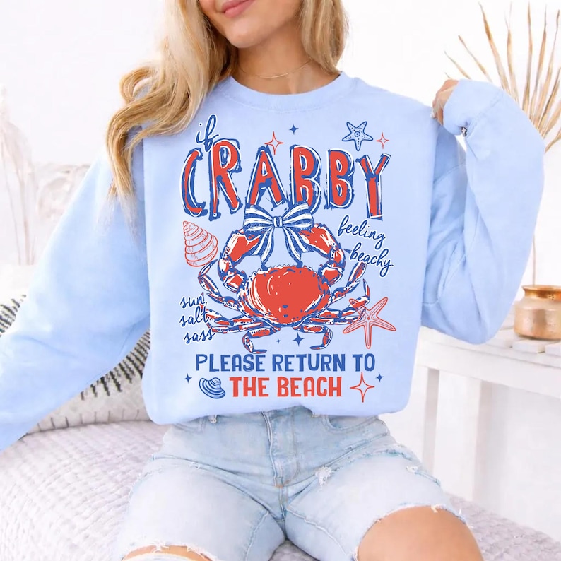 May include: Light blue sweatshirt with a crab graphic. The graphic includes a red crab with a blue bow, seashells, and the text "If Crabby Feeling Beachy Please Return to the Beach."
