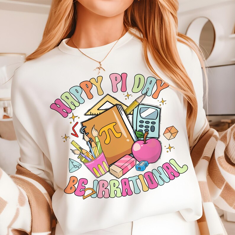 May include: White sweatshirt with a colorful graphic design that says "Happy Pi Day Be Irrational". The graphic includes a notebook with a pi symbol, pencils, a calculator, a protractor, a ruler, and an apple.