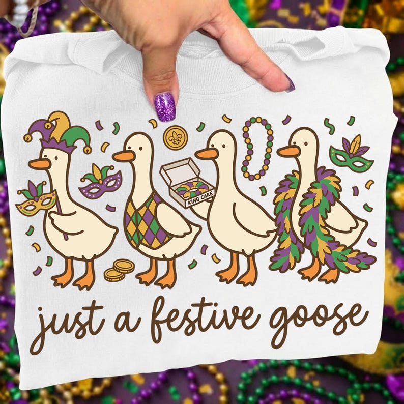 Op de afbeelding: Wit T-shirt met een ontwerp van vier cartoon ganzen in feestelijke kleding, inclusief maskers, kralen en een koningscake. De tekst "just a festive goose" staat eronder. Het ontwerp gebruikt paars, groen, goud en oranje.