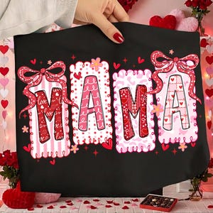 May include: Black tote bag with the word "MAMA" in large, decorative letters. Each letter is a different pattern of pink and red, with bows and hearts. The background is black.