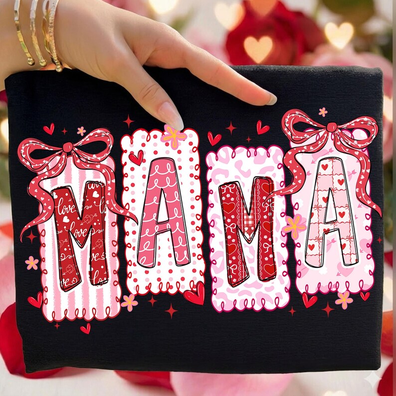 May include: Black t-shirt with the word "MAMA" in large, decorative letters. Each letter is a different pattern of red and pink, with scalloped edges and bows. Hearts and flowers are scattered around the letters.