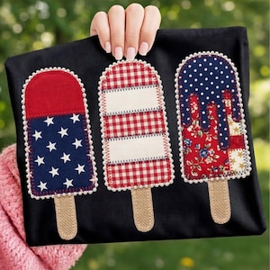 May include: A black tote bag with three decorative popsicle patches. The patches feature red, white, and blue patterns, including stars, polka dots, and gingham. Each popsicle has a burlap stick and a scalloped edge.