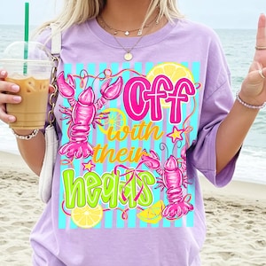 May include: A lilac t-shirt with a graphic design. The design features two pink lobsters, lemon slices, and the text "Off with their heads" in pink and green. The design is set against a blue and white striped background.