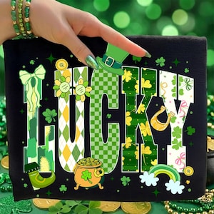 Pode incluir: Camiseta preta com a palavra "LUCKY" em um design colorido com tema do Dia de São Patrício. As letras são decoradas com trevos, um pote de ouro, um arco-íris e um chapéu de duende. O design incorpora cores verde, amarelo e branco.