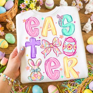 May include: White Easter sweatshirt with colorful text and graphics. The word "EASTER" is displayed in bubble letters with a cross, bow, egg, and bunny illustrations. Decorative Easter eggs and bunnies surround the sweatshirt.