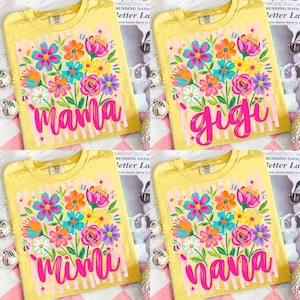 Könnte beinhalten: Gelbe T-Shirts mit Blumendesigns und den Wörtern "Mama", "Gigi", "Mimi" und "Nana" in leuchtendem Pink. Die floralen Arrangements umfassen rosa, blaue, orange und weiße Blumen mit grünen Blättern. Vertikale rosa Streifen und Sterne umrahmen den Text.