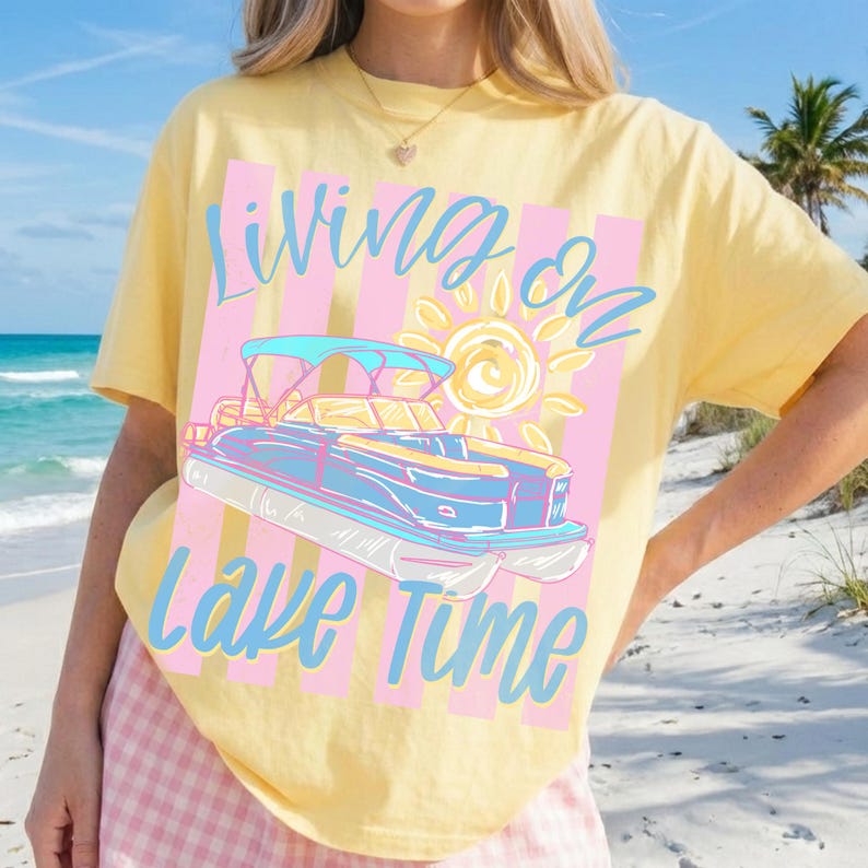 May include: Yellow t-shirt with a graphic of a pontoon boat, sun, and text "Living on Lake Time" in blue. The design is set against pink and white vertical stripes. The shirt is a casual wear item.