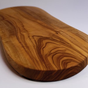 May include: A wooden chopping board with a natural, organic shape. The board is made of light brown wood with darker brown grain patterns. The surface is smooth and appears well-finished, suitable for food preparation.