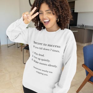 Puede incluir: Sudadera blanca con el texto "Secret to success: If you fall down 7 times, 1. Play dead. 2. Get up quietly. 3. Make moves silently. Someone nearby was tripping you."