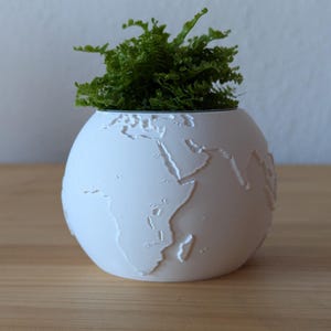 Könnte beinhalten: Eine weiße Keramik-Tasse mit schwarzem Henkel und dem Text "But First, Coffee" in fetter, schwarzer Schrift. Die Tasse ist mit einer dunklen Flüssigkeit gefüllt, wahrscheinlich Kaffee, auf einer hellen Oberfläche.