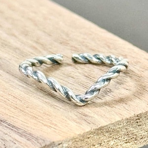 May include: A silver ring with a twisted rope design. The ring is open and adjustable.