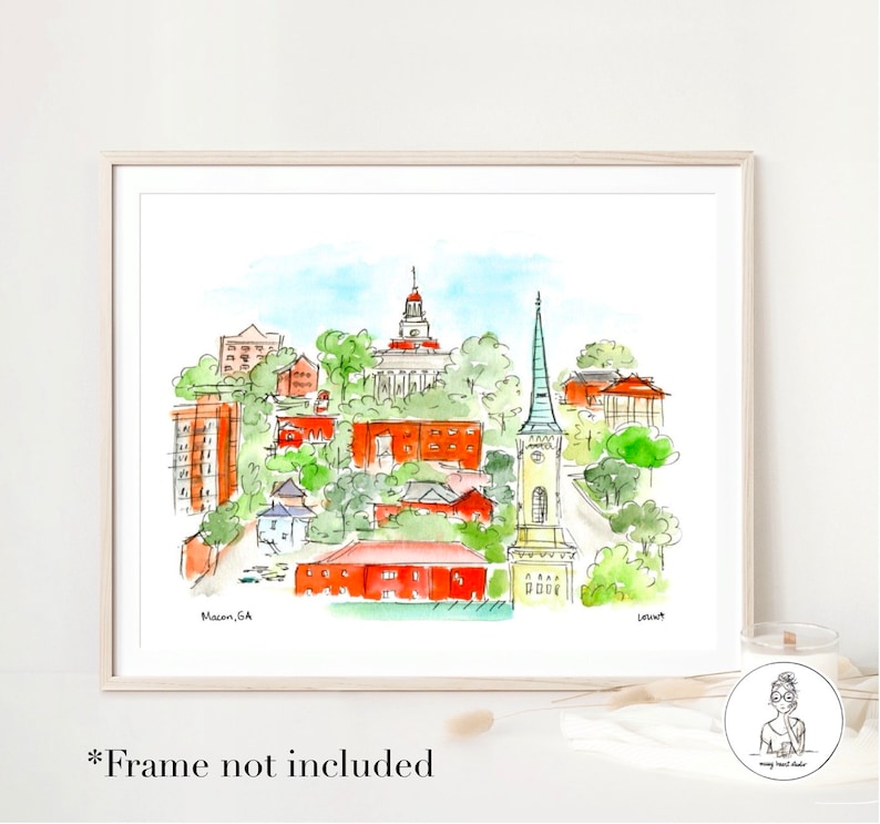 Op de afbeelding: Waterverfillustratie van de skyline van Macon, Georgia, met een hoge kerktoren, een rood bakstenen gebouw met een koepel en andere gebouwen en bomen. De tekst "Macon, GA" staat in de linkerbenedenhoek van de afbeelding.