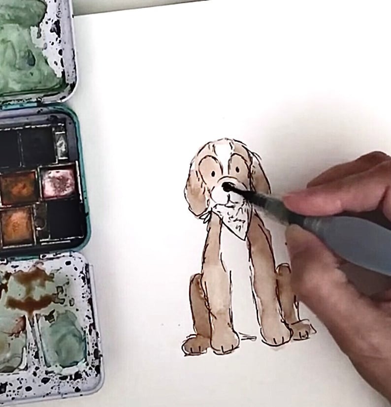 May include: A hand paints the nose of a brown and white dog illustration with a black watercolor brush. The dog is sitting with its legs crossed and has a white bandana around its neck.
