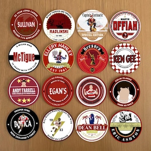May include: Sixteen circular coasters with different designs and text, featuring names such as Sullivan, Radlinski, and McTigue. The coasters display team logos and phrases, with a color scheme mainly of red, white, and black. The coasters are on a wooden surface.