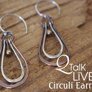 May include: A pair of silver and copper earrings with a teardrop shape. The earrings have a double loop design and a small gold bead hanging in the centre.