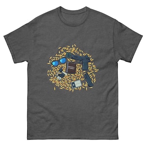 Puede incluir: Camiseta gris oscuro con un diseño de una pistola, gafas de sol, un libro pequeño, una bandera de Texas y llaves, todo rodeado de balas. La camiseta está hecha de un material suave y cómodo.