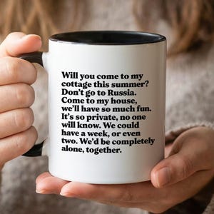 Pode incluir: Uma caneca de cerâmica branca com interior e alça pretos, com texto preto. O texto diz: "Você vem para minha casa de campo neste verão? Não vá para a Rússia. Venha para minha casa..." A caneca é segurada por uma pessoa.