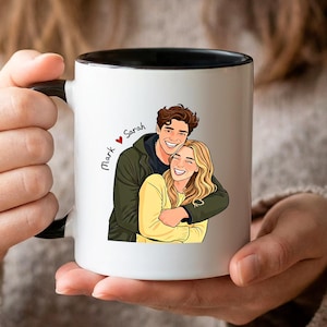 Könnte beinhalten: Weißer Keramikbecher mit schwarzem Innenraum und Henkel, mit einer Cartoon-Illustration eines sich umarmenden Paares. Der Becher trägt die Namen "Mark" und "Sarah" mit einem Herzsymbol. Das Paar trägt Freizeitkleidung.