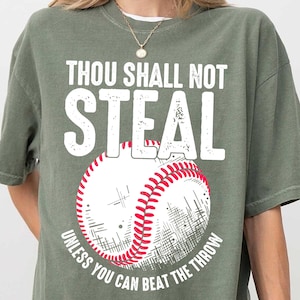 Op de afbeelding: Groen T-shirt met een witte baseball-afbeelding en de tekst "Thou Shall Not Steal Unless You Can Beat The Throw".