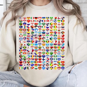 May include: A cream-colored sweatshirt featuring a large graphic of numerous heart-shaped flags from around the world. The flags are arranged in a grid pattern, showcasing a variety of colors and designs. The sweatshirt has a crew neck and long sleeves.