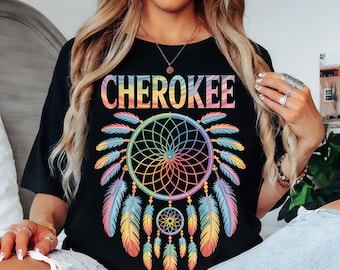 May include: Black t-shirt featuring the word "CHEROKEE" in rainbow colors above a dreamcatcher design. The dreamcatcher has a rainbow web and colorful feathers in shades of blue, yellow, and pink.