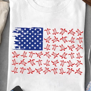 May include: A white t-shirt with a red, white, and blue American flag design. The flag is made up of red sea turtles.