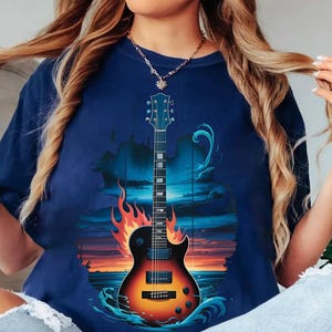A woman wearing a blue t-shirt with a graphic design of a guitar and flames, with her hair in motion.