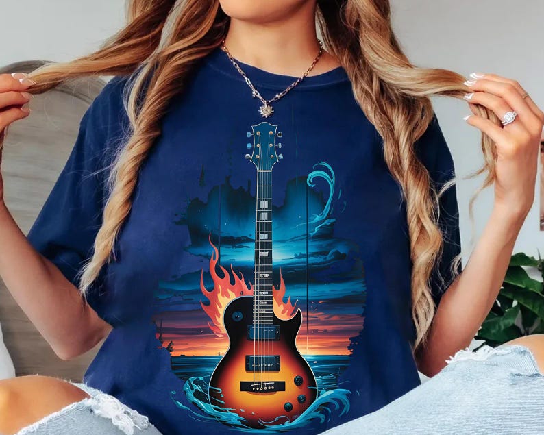 A woman wearing a blue t-shirt with a graphic design of a guitar and flames, with her hair in motion.