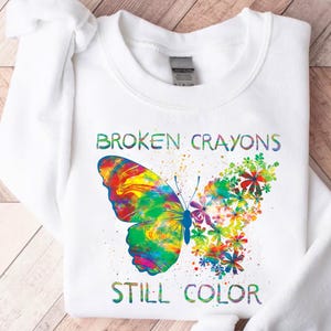 May include: White sweatshirt with a colorful butterfly and the text "Broken Crayons Still Color".