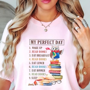May include: Pink t-shirt featuring a graphic of an owl reading a stack of books. The text on the shirt reads "My Perfect Day" and lists activities including "Read Books" multiple times.