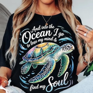 Puede incluir: Camiseta negra con un diseño de tortuga marina colorida y el texto "And into the Ocean I go to lose my mind & find my Soul". La tortuga tiene un caparazón arcoíris y está rodeada de agua azul.