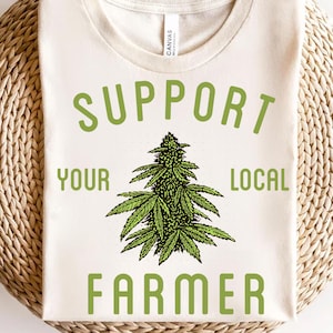 May include: A white t-shirt with a green graphic of a marijuana plant and the text "Support Your Local Farmer".