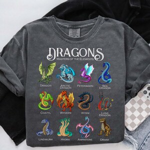 May include: Dark gray sweatshirt featuring a variety of colorful dragon illustrations. The word "DRAGONS" is printed at the top, with "MASTERS OF THE ELEMENTS" below. Each dragon is labeled with its name, including Dragon, Arctic Dragon, and Sea Dragon.