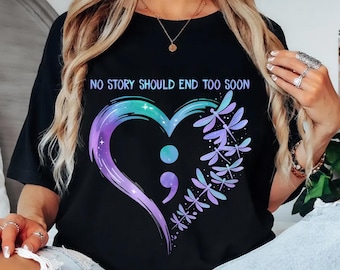 May include: Black t-shirt with the text "NO STORY SHOULD END TOO SOON". The shirt features a heart-shaped design with a semicolon, a dragonfly, and a gradient of purple, teal, and blue colors.