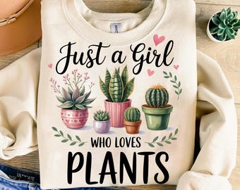 May include: Cream-colored sweatshirt with the text "Just a Girl Who Loves Plants" and illustrations of potted succulents and cacti. The design includes pink hearts and green foliage, creating a botanical theme.