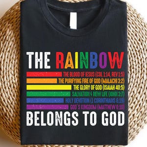 Puede incluir: Camiseta negra con diseño de arcoíris y el texto "THE RAINBOW BELONGS TO GOD". El arcoíris está compuesto por franjas de colores con versículos bíblicos. Una prenda casual e inspiradora.