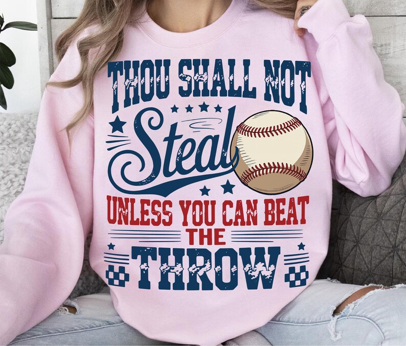 a pink sweatshirt with a graphic design that includes a baseball and text.