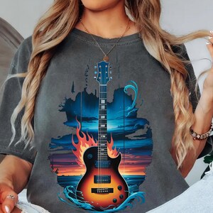 A woman wearing a gray t-shirt with a graphic design of a guitar and a sunset in the background.