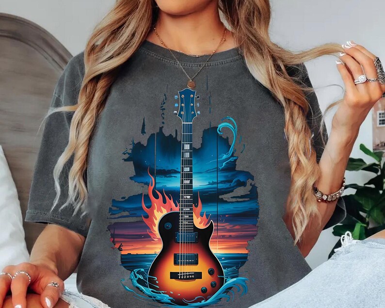 A woman wearing a gray t-shirt with a graphic design of a guitar and a sunset in the background.