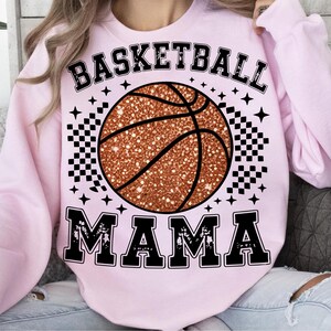 A woman wearing a pink sweatshirt with a basketball graphic and the text "BASKETBALL MAMA" printed on it.