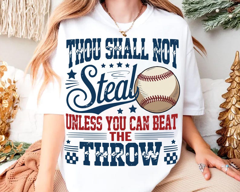 A white t-shirt with a graphic design featuring a baseball and text that reads "THOU SHALL NOT STEAL UNLESS YOU CAN BEAT THE THROW".