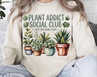 May include: Cream-colored sweatshirt featuring the text "PLANT ADDICT SOCIAL CLUB - JUST ONE MORE PLANT" above a watercolor illustration of potted succulents and other plants. The design includes various shades of green and brown.