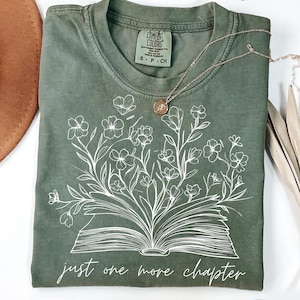 May include: A green t-shirt with a white design of an open book with flowers growing out of it. The text "just one more chapter" is printed below the book.