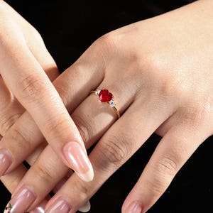May include: A gold ring with a red heart-shaped gemstone and two smaller clear gemstones.