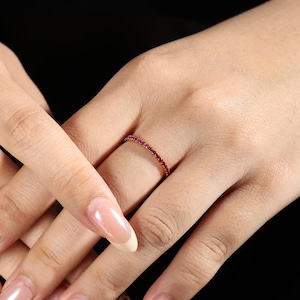 Puede incluir: Un delicado anillo con una fila continua de pequeñas y vibrantes piedras preciosas rojas. El anillo está engastado en una banda delgada, creando un diseño minimalista y elegante. Las piedras preciosas están espaciadas uniformemente, mostrando un color y brillo consistentes.
