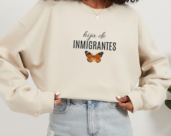 May include: A beige sweatshirt with the text "hija de INMIGRANTES" and a butterfly graphic.
